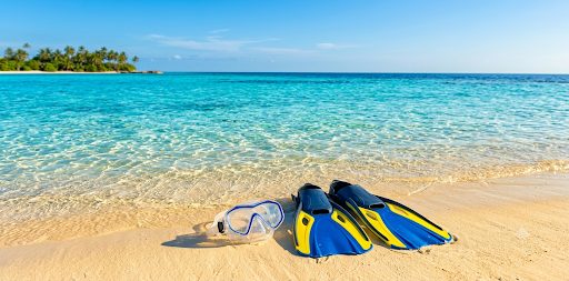 Masque de snorkeling et palmes posés sur le sable doré au bord d'une mer turquoise cristalline